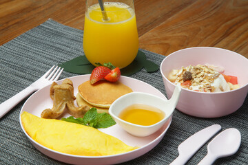 Kids menu - omlet, pancakes with maple syrup, muesli with yoghurt and glass of fresh squuzed orange juice served on the restaurant table with plastic kids friendly eating utensil.