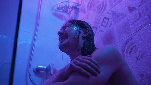 Man crying in the shower under running water in neon light, lingering depression