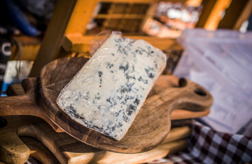 A piece of French cheese with blue mould on a wooden board being sold