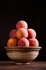 Red-yellow peaches on clay bowl on a rustic wooden table against dark background