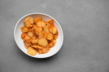 Organic Cassava chips in white bowl on gray background. Indonesia popular hot spicy snacks. Keripik singkong. View from above. Copy space.