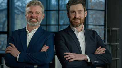 Two successful smiling businessmen posing together with crossed arms young and mature man business...