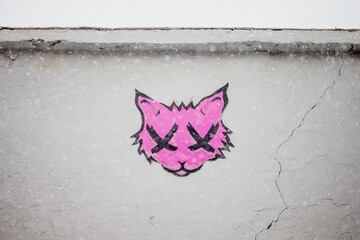 Creative pink cat graffiti on side of grey wall during snowing