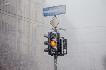 Yellow middle light in snowy traffic light during heavy snow fall in middle of the city