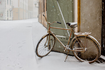 Fototapeta na wymiar Brown vintage metal bike parked in old town Riga during snow fall covered by snow flakes in winter
