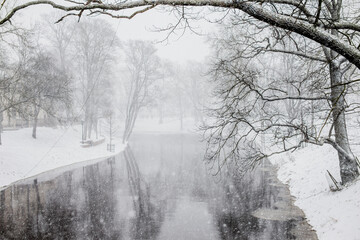 Calm mirroring water surface canal in snowy park in middle of city