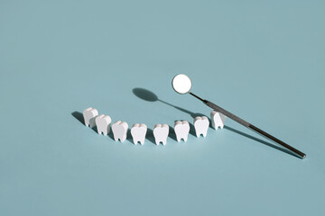 Steel dental mirror for examination of teeth and oral cavity and models of snow-white teeth standing hardly on a blue background