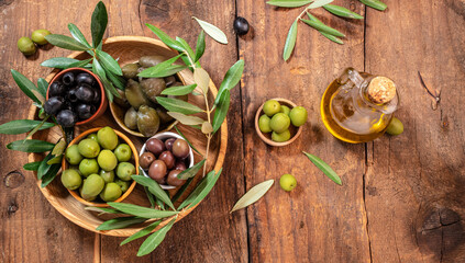 olives berries in wood bowls and oil in glass bottles on a wooden background. Healthy and detox...