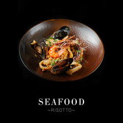 Seafood risotto served on copper plate isolated on black background. Italian rice risotto with...