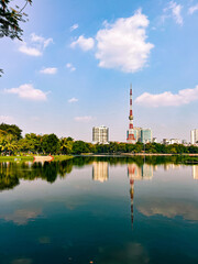 Radio tower in a city centre of Hanoi, Vietnam with a reflection over a lake during a sunny day with couple of clouds