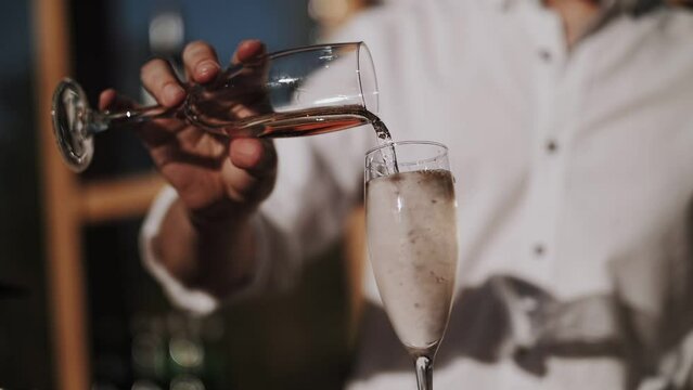 Bartender pours cocktails into glasses. Bar in the open space.