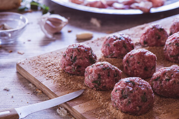 Raw meatballs and a knife on a wooden cutter on a kitchen table