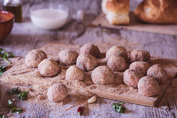 Homemade Meatballs on a wooden cutter on a kitchen table with bread, milk and breadcrumbs 