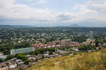 Obraz premium Panoramic top view of the city of Pyatigorsk in the Stavropol territory with residential buildings among green trees and cloudy sky in a haze on a summer day and space for copying
