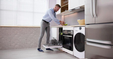 Happy Man Arranging Plates In Dishwashing Machine