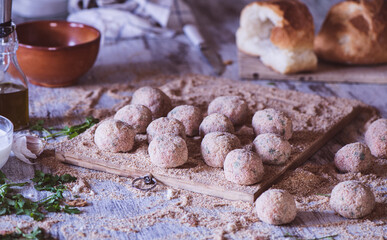 Meatballs covered in breadbrumbs and other ingredients on a kitchen table
