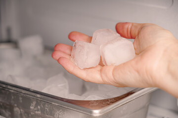 The girl takes frozen ice cubes from the freezer with her hand to prepare soft drinks.