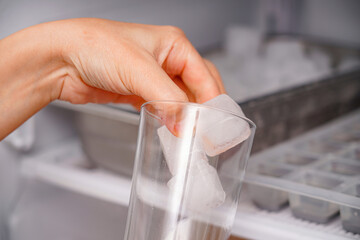 The girl collects frozen ice cubes in a glass goblet from the freezer.