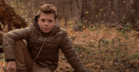 Boy sits on the wooden bridge over the river in fall forest. Brown toned.