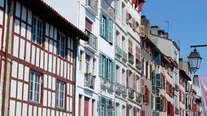 Fototapeta na wymiar Colourful vintage facades of typical french basque homes with shutters and windows of faded colours downtown in Bayonne, Basque country, Spain. Panoramic view