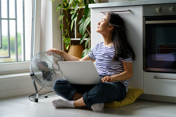Carefree positive Asian female copywriter working sits in kitchen on floor with laptop and pointing...