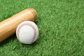 Wooden baseball bat and ball on green grass, closeup. Space for text