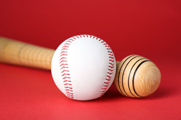 Wooden baseball bat and ball on red background, closeup. Sports equipment