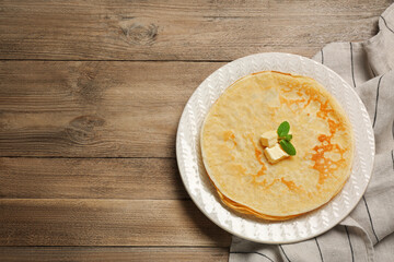 Stack of delicious crepes with melting butter and mint on wooden table, top view. Space for text