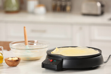 Cooking delicious crepe on electric pancake maker in kitchen. Space for text
