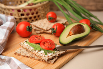 Fresh crunchy crispbreads with cream cheese, tomatoes and avocado on beige table