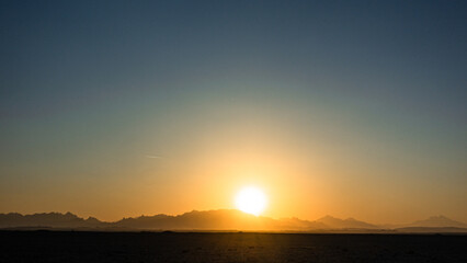 Naklejka na ściany i meble Beautiful clear big sun at sunrise or sunset against the backdrop of mountains. Africa.