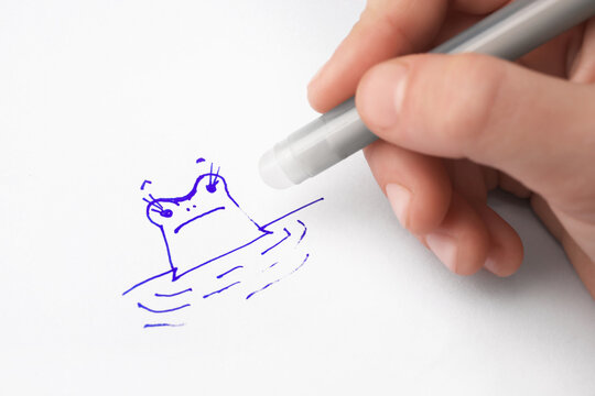 Child erasing drawing with erasable pen on paper sheet, closeup