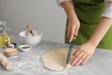 Woman cutting dough at light grey marble table, closeup. Cooking grissini