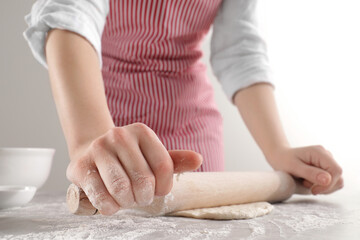 Woman rolling fresh dough at light grey table, closeup. Cooking grissini
