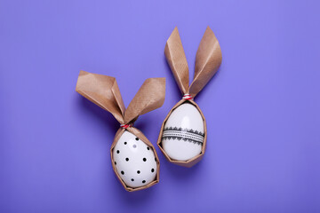 Easter bunnies made of craft paper and eggs on purple background, flat lay