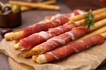 Delicious grissini sticks with prosciutto on table, closeup