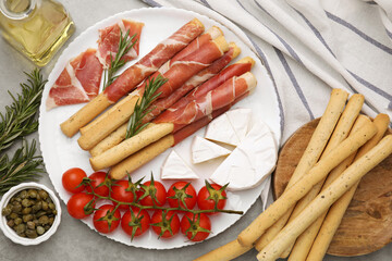 Delicious grissini sticks with prosciutto and snacks on grey table, flat lay
