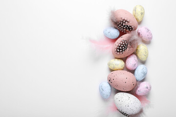 Many painted Easter eggs with feathers on white background, flat lay. Space for text