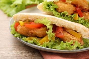 Delicious pita sandwiches with fried fish, pepper, tomatoes and lettuce on wooden table, closeup