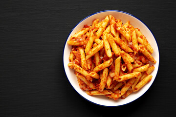 Homemade Penne With Tomato Sauce on a Plate on a black background, top view. Space for text.