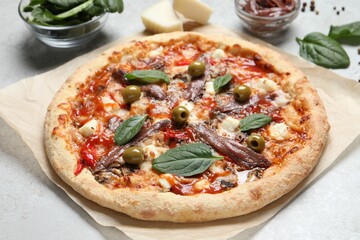 Tasty pizza with anchovies and ingredients on white table