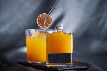 glass jar with orange drink, in the background a glass with ice and dried fruit on a gray cloth...