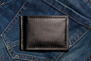 Black handmade leather wallet on blue jeans. Male background. View from above.