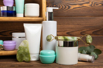 Skin care cosmetics on a brown wooden table. Cosmetic tubes in the bathroom. Facial cream and serum, facial wash, quartz gua sha and face roller. Facial care concept. MOCAP.