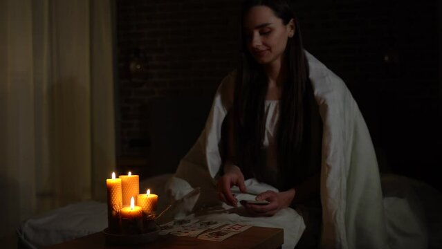 A woman fortune-telling with cards in a dark room by the light of burning candles. Image of candles in sharpness, playing cards and a woman out of focus.