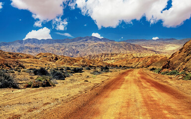 Beautiful red desert landscape, empty dirt road track into valley, arid rugged hills and mountains...