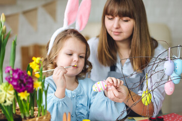 Obraz premium Beautiful mother and cute daughter are spending quality time together, making craft handmade eggs for Easter home decoration. Spring flowers, cozy holiday atmosphere , family traditions and values