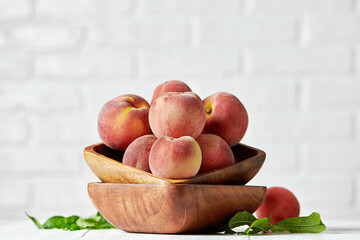 Peaches in wooden bowl with white brick wall background