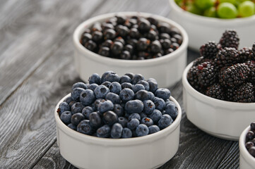 Fototapeta na wymiar Ripe blueberries on the table in a plate, among the assortment of ripe berries, raspberries, blueberries, gooseberries, currants, shot close-up