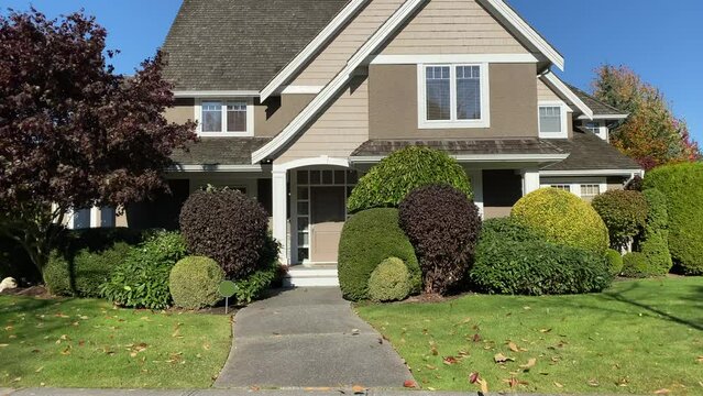 Establishing shot of two story stucco luxury house with garage door, big tree and nice Fall Foliage landscape in Vancouver, Canada, North America. Day time on Sept 2021. ProRes 422 HQ.